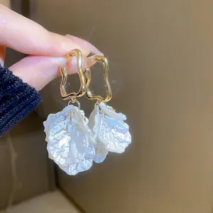 Gros plan de boucles d'oreilles pétales dorées tenues à la main pour un look élégant
