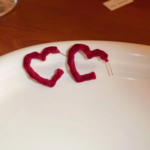 Detail of red heart-shaped velvet earrings placed in a white porcelain dish on wood