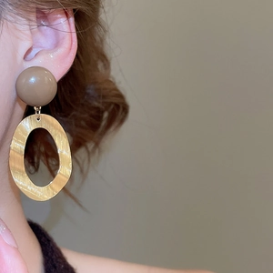 Close-up of model wearing oval brushed metal earrings with brown resin bead detail