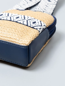 Woven straw crossbody bag with dark blue faux leather trim and geometric pattern strap