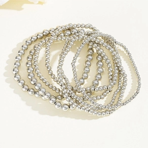 Set of silver beaded stretch bracelets with layered geometric metal beads on beige background