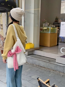 Detail of white plush shoulder bag with a large red plaid bow in an outdoor cafe setting