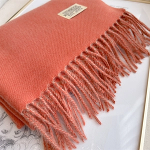 Detailed close-up of coral orange cashmere-like scarf with fringe and brand label