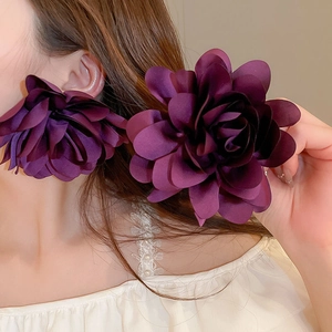 Detail view of large purple fabric flower earrings shown on a model for vacation style