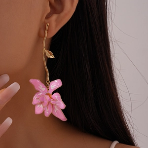 Close-up of pink enamel flower earrings with long gold branches worn by a model