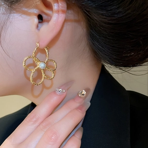 Detail shot of golden metal hollow flower earring with pearl center on a model ear