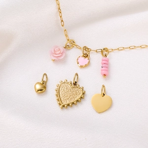 Detailed view of pink heart and rose charms on a gold chain over white silk background