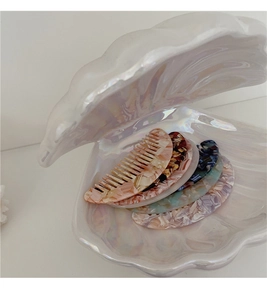 Close-up of mini acetate hair combs with marble texture in a pearlescent shell tray