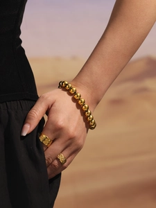 Close-up of polished gold bead bracelet and embossed rings on a hand against desert sand