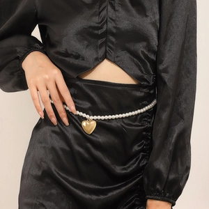 Detail view of heart-shaped gold pendant on white pearl waist chain over black dress