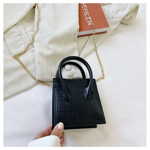 Detail of black crocodile texture mini bag with gold chain strap on stylish background