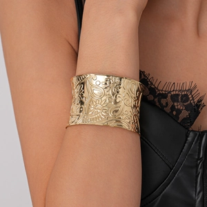 Close-up of golden wide cuff bracelet with intricate floral and paisley embossed patterns