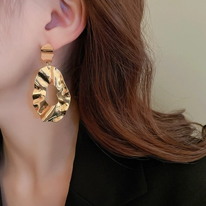 Macro shot of large golden irregular textured earrings worn on a female model