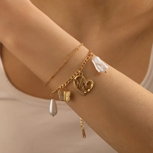 Détail d'un bracelet doré multicouche avec papillon, perle et breloque coeur pour maman