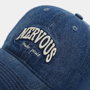 Close-up of 3D white embroidery on dark blue washed denim baseball cap with logo detail