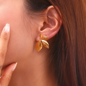 Polished 18K gold plated stainless steel leaf stud earrings worn by a female model