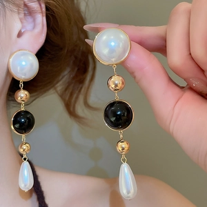 Detail of 18k gold plated drop earrings with white pearls and black beads on a model
