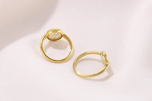 Close-up of golden geometric ring with white floral zircon cluster on pink fabric