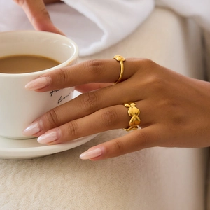 Detail of gold heart-shaped stackable rings on hand holding a coffee cup