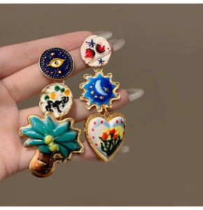 Detail of asymmetrical gold-plated enamel earrings featuring star, moon and heart patterns