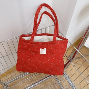 Detail of red quilted tote bag with white rabbit embroidery inside a metal cart