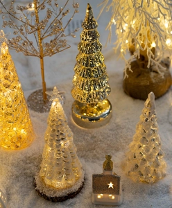 Macro shot of glowing LED glass Christmas tree with gold mercury finish on snow base