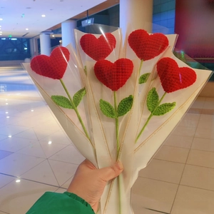 Detail showing five hand-crocheted red heart-shaped flowers with green leaves