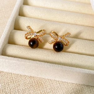 Macro shot of gold bow stud earrings with tiger eye stone drop in a jewelry box