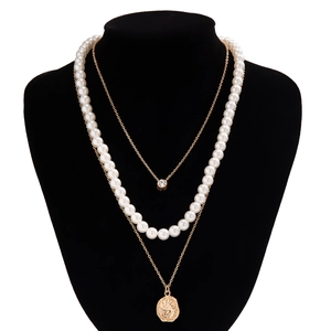 Detail van gelaagde ketting met witte parels, gouden munt hanger en ronde kristal steen
