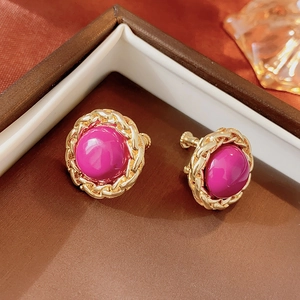 Detail of vintage round gold chain-wrapped earrings with a magenta resin center stone