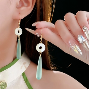 Detailed shot of resin water drop earrings with white round jade-like studs and gold hooks