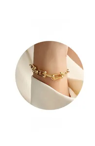 Dettaglio del bracciale a maglie a U dorate in stile industriale su sfondo di seta bianca