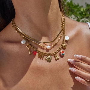 Gold-layered necklace with key strawberry heart and bow charms worn outdoors