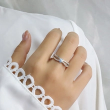 Close-up of a silver hollow cross ring with a blue gemstone on a model's finger