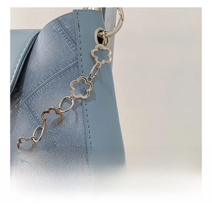 Detail of light blue textured bag featuring golden flower-shaped hardware chain links