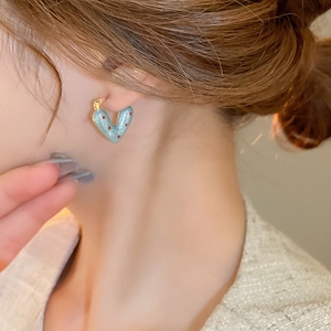 Close-up of heart-shaped earring with red polka dots on blue enamel worn by a model