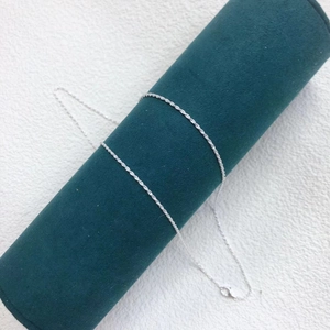 Detail of a thin silver water wave chain necklace wrapped on a green velvet jewelry roll