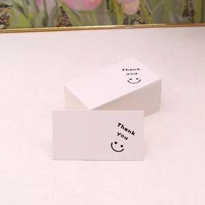 Close-up of white paper earring cards with Thank You text and smiley face patterns