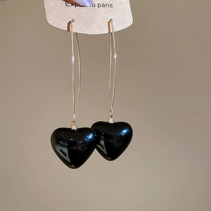 Detailed shot of unique black heart-shaped pearl drop earrings on a paper display card