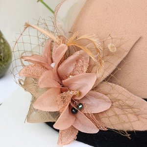 Detailed close-up of decorative silk flower, mesh veil, and feathers on a wool felt hat