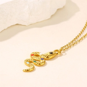 Gold snake pendant necklace with colorful gemstones on a minimalist white stone background