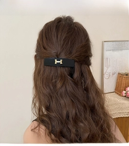 Close-up of geometric acrylic hair clip featuring a gold letter H on black base