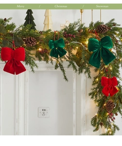 Detail of red and green velvet Christmas bows hanging on a festive pine branch with lights