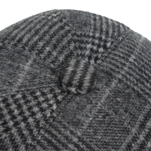 Detail view of winter flat cap showing grey-black plaid wool texture and top button