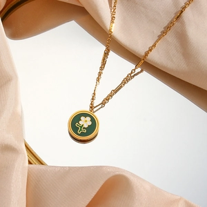 Macro detail of 18K gold-plated necklace with green enamel floral pendant on silk fabric