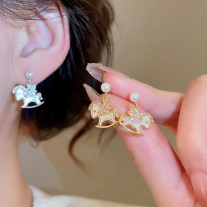 Close-up of gold rocking horse earrings with pearls and shimmering zircons detail