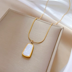 Macro shot of gold square shell pendant on sleek snake chain over silk fabric