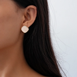 Close-up of golden square stud earring with white marble enamel finish on model ear