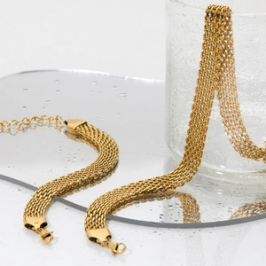 Golden 10mm mesh chain necklace and bracelet set displayed on a reflective water surface