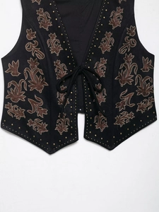 Detail of floral embroidery and metallic studs on black V-neck suede vest with lace-up front